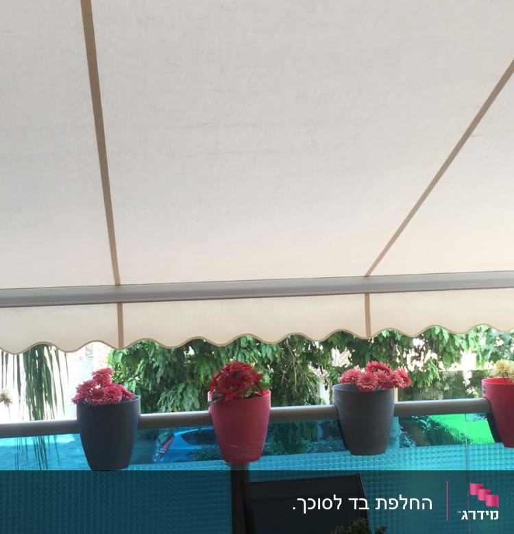 סוכך לבן מתוח מעל מרפסת עם עציצים.